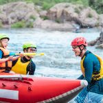 Family of three playing with water pistols near inflatable rowing catamaran