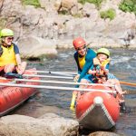 Family of three playing with water pistols while sitting on inflatable rowing catamaran