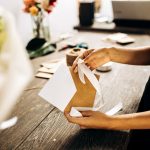 Florist is packing a postcard in an envelope with white ribbon on the wooden table