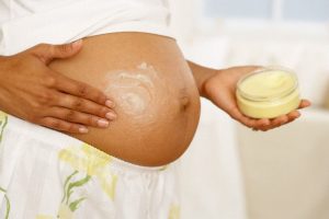 Pregnant woman rubbing stretch mark cream on stomach --- Image by © DK Limited/Corbis