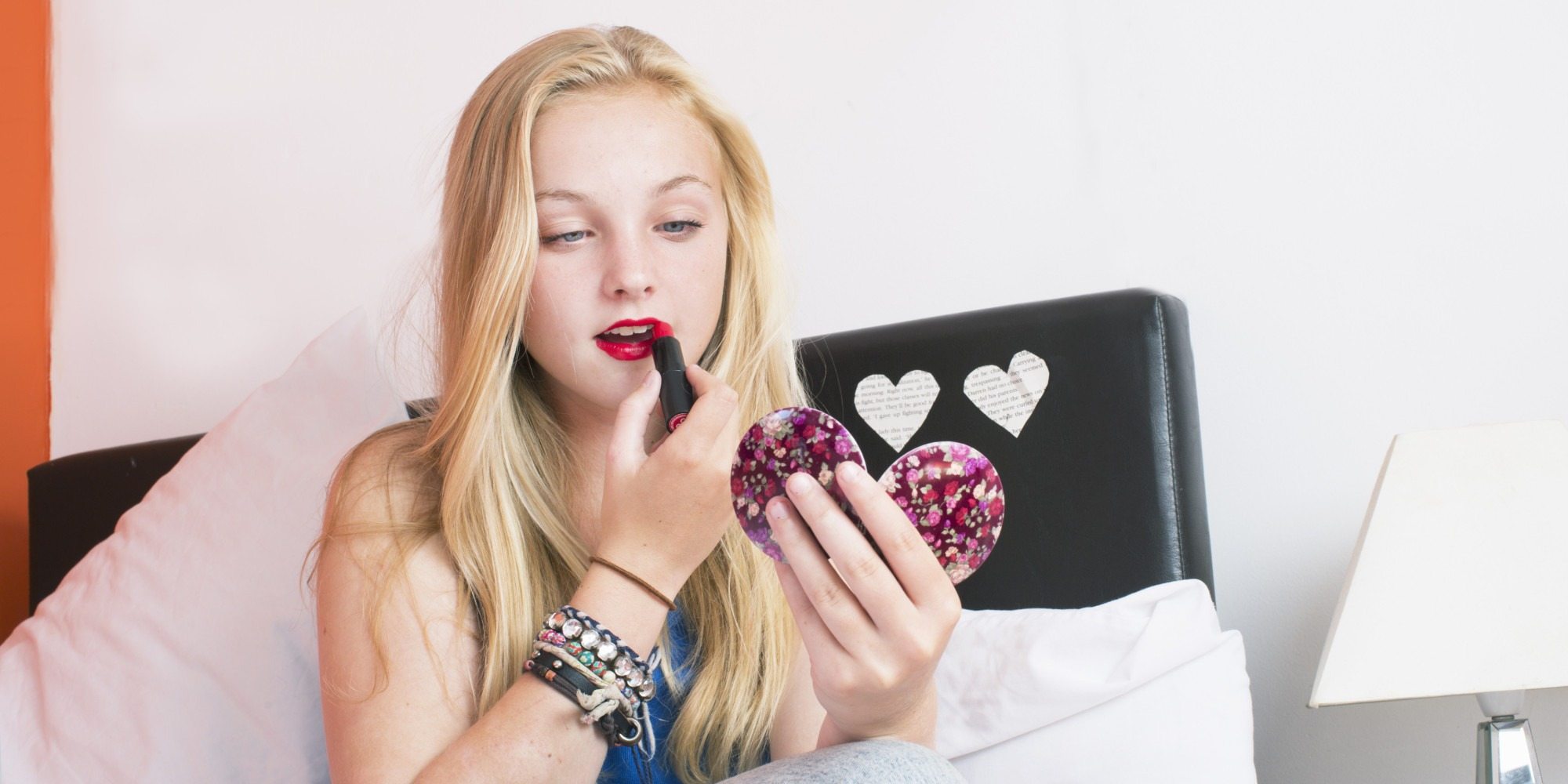 teenage girl in her bedroom putting on lipstick