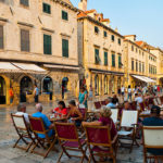 Panoramic photo of Stradun, the famous street in Dubrovnik, tourists in a cafe by the City Bell Tower, Dubrovnik, Dalmatia, Croatia