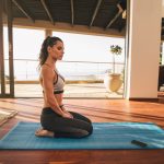 Beautiful young woman sitting in yoga pose at home