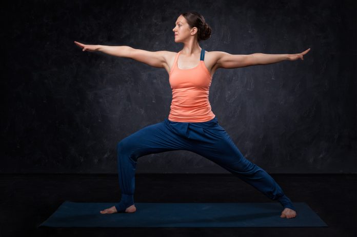 Woman practices yoga asana utthita Virabhadrasana