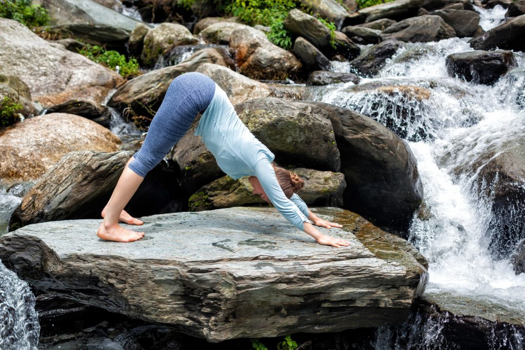 Young fit woman doing yoga oudoors at waterfall