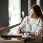 Beautiful woman sitting in restaurant and writing