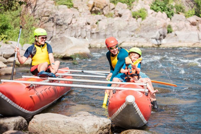 Family of three playing with water pistols while sitting on inflatable rowing catamaran