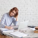 Woman freelancer female hands with pen writing on notebook at home or office