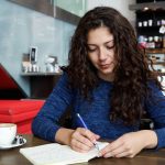 Young woman sitting at coffee shop table and writing a book