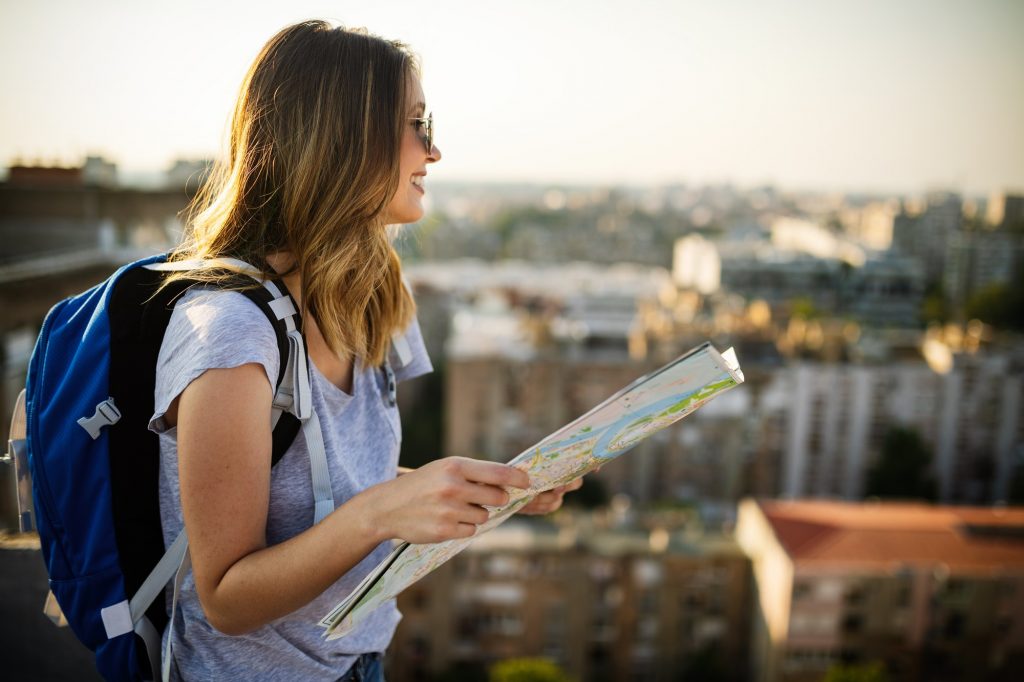 Happy female tourist searching road to hotel on map in city during vacation