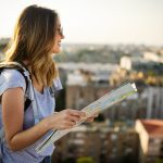 Happy female tourist searching road to hotel on map in city during vacation
