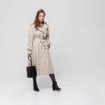 Beautiful woman with wavy hair in striped coat holding black bag thoughtfully looking in camera