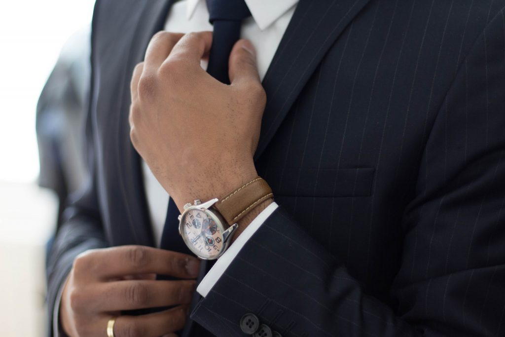 Man in suit with watch adjusting cufflinks.