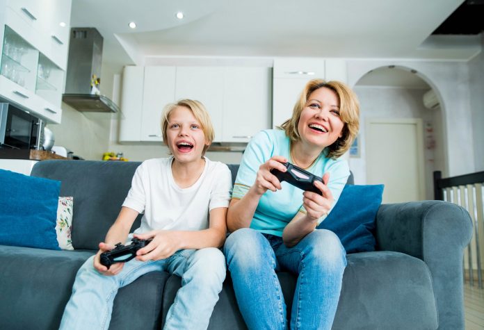 Child son and mother playing video games together at home