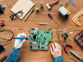 cropped image of electronic engineer with robotic hand fixing motherboard by soldering iron at table