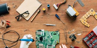 cropped image of electronic engineer with robotic hand fixing motherboard by soldering iron at table