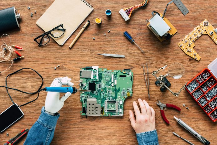 cropped image of electronic engineer with robotic hand fixing motherboard by soldering iron at table