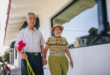 elderly couple holding hands and holding red flowers while walking