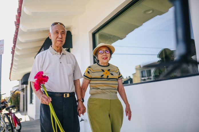 elderly couple holding hands and holding red flowers while walking