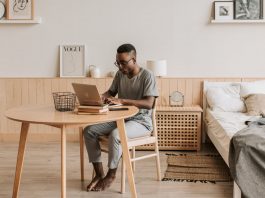 man in gray crew neck t shirt and blue denim jeans sitting on white couch using