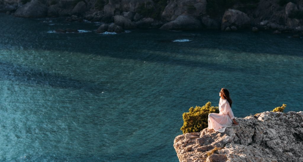 Beautiful girl sitting on a high rock and looking out to sea, panorama