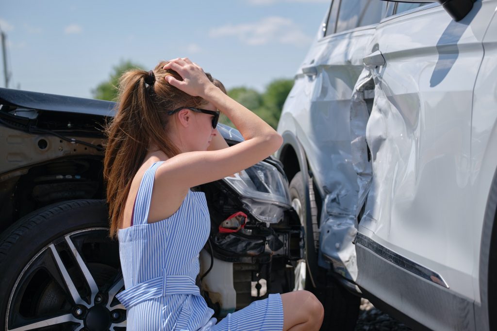 Stressed woman driver sitting on street side shocked after car accident. Road safety and insurance