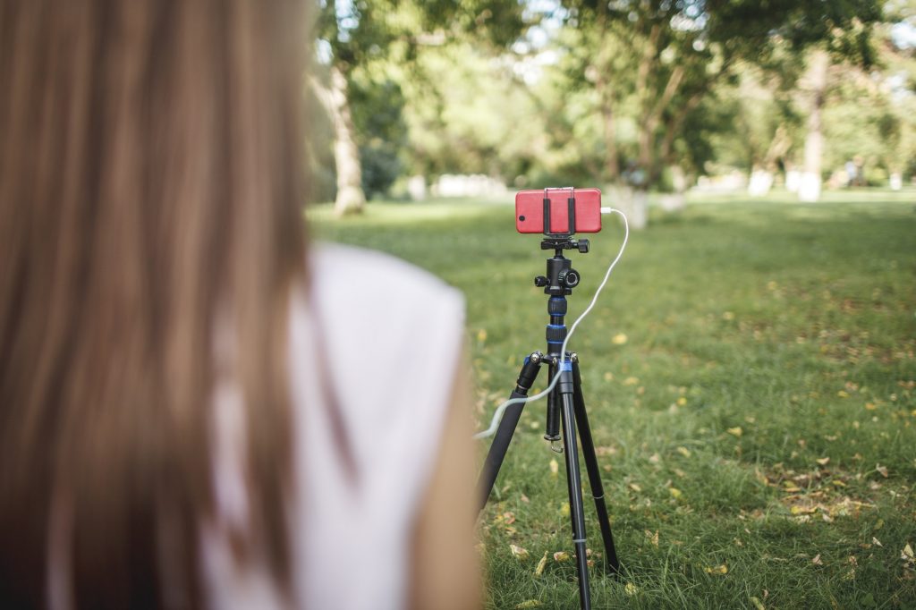 Woman working with camera phone on tripod on a meadow