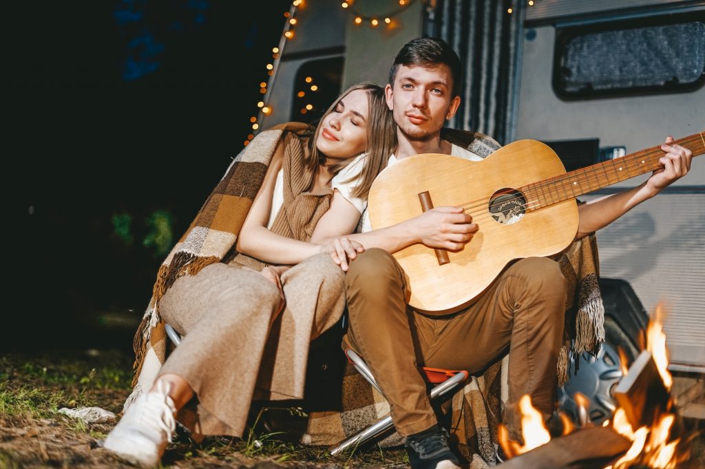 Young couple in love in cozy warm stylish outfit with gitar near fireplace romantic weekend against