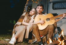 Young couple in love in cozy warm stylish outfit with gitar near fireplace romantic weekend against