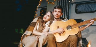 Young couple in love in cozy warm stylish outfit with gitar near fireplace romantic weekend against
