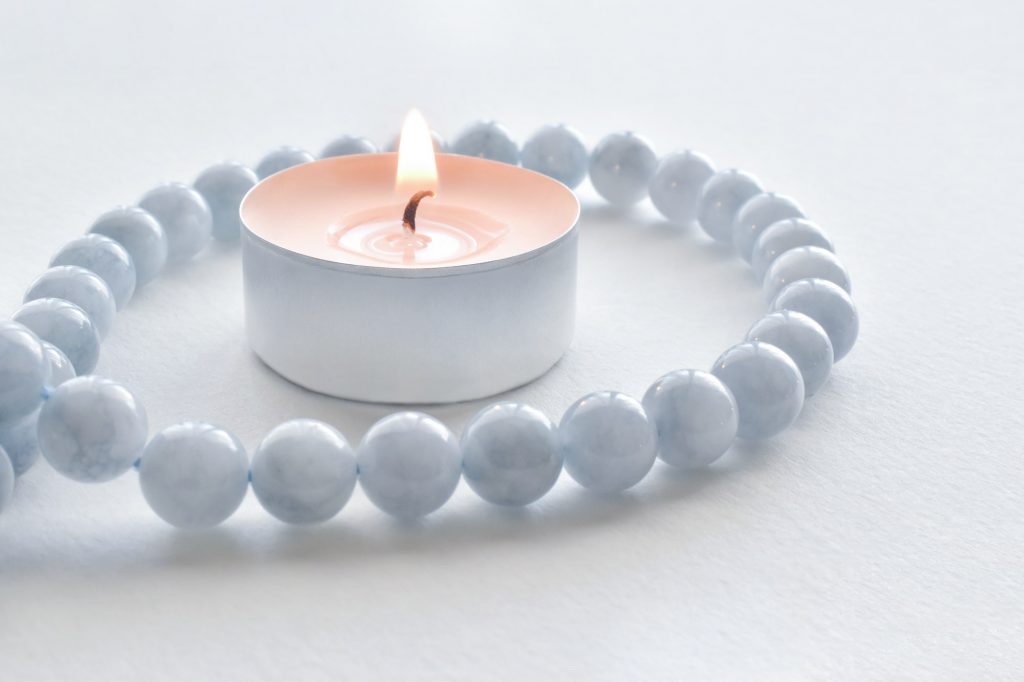 Tealight candles with aquamarine necklace around it on the table.