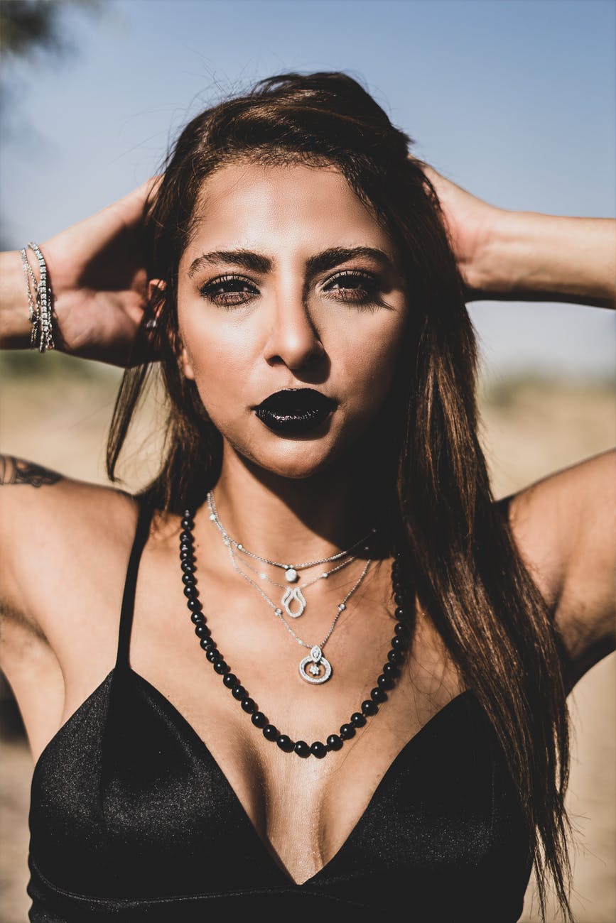 portrait of a woman wearing black lipstick and bikini on a beach while holding her hands in hair