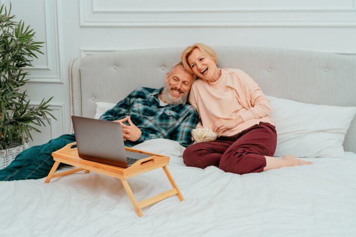 Husband and wife watch a film on the bed and eat popcorn