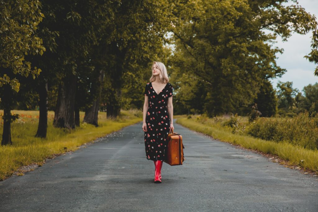 Blonde girl in red boots with suicase at countryside road