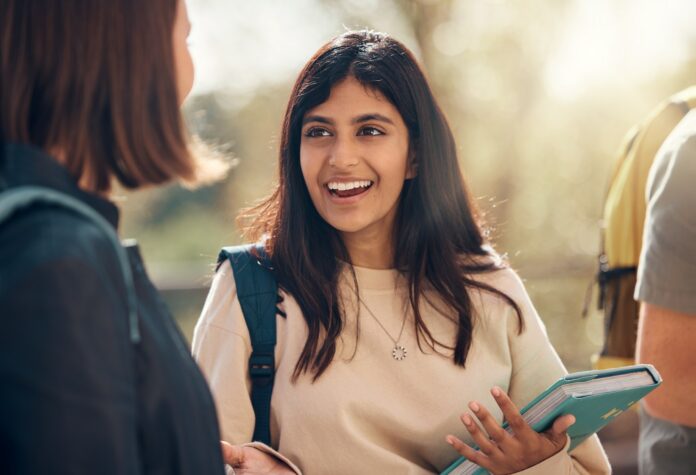 Happy, university and woman student from India laughing and talking about a test. College, book and
