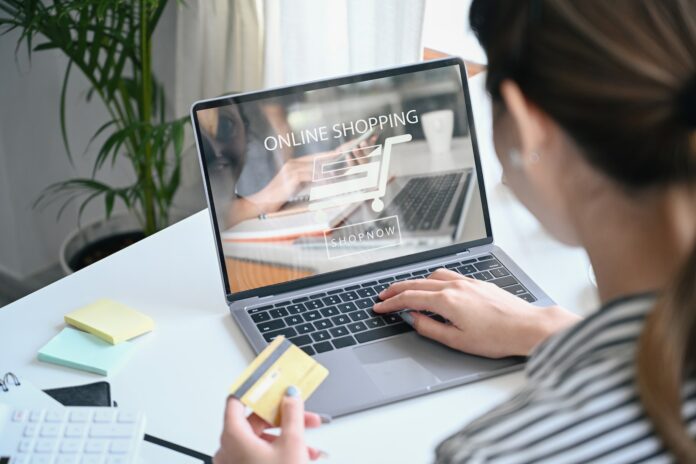 View over shoulder young woman holding credit card and shopping online on E-commerce website.