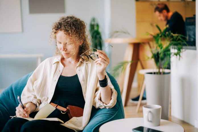 Woman puts on glasses and writes in paper notebook