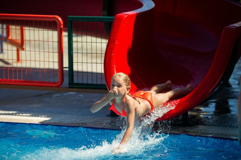 A little girl slides down a water slide into a pool in a water park during the summer holidays