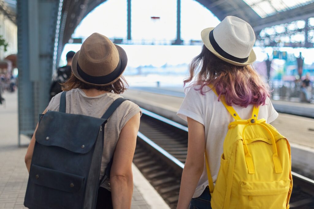 Two women mother and teenage daughter walking with luggage at railway station