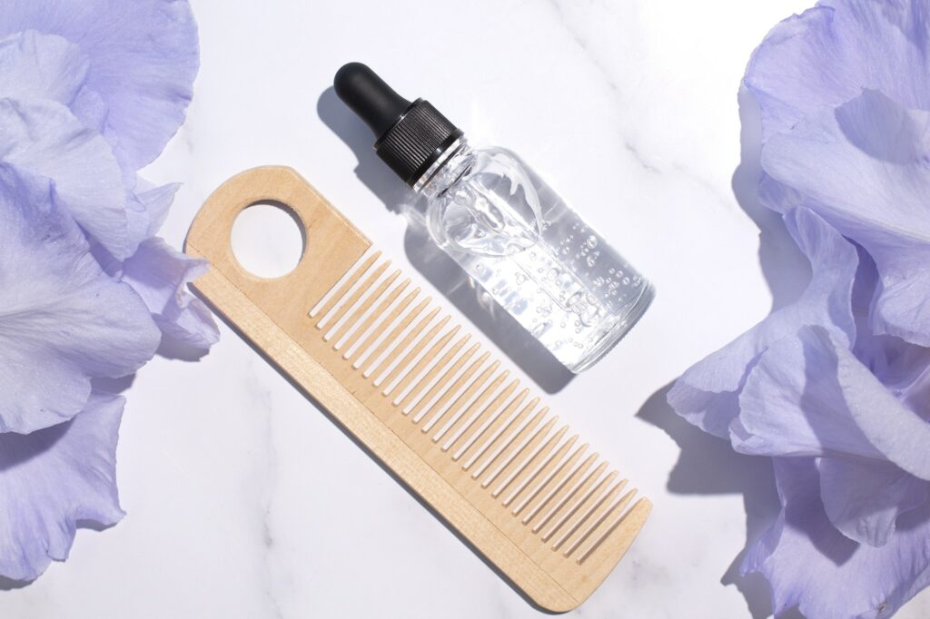 Glass bottle with serum, wooden hair comb on marble background with iris flowers