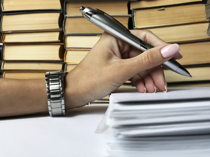 Female Hand With Manicure and Wrist Watch Hoding Silver Pen Over Document Package