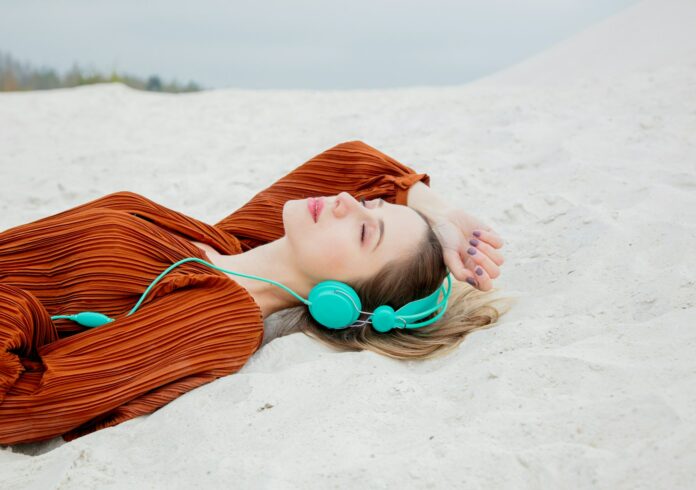 Young woman in burgundy color blouse with headphones lying down